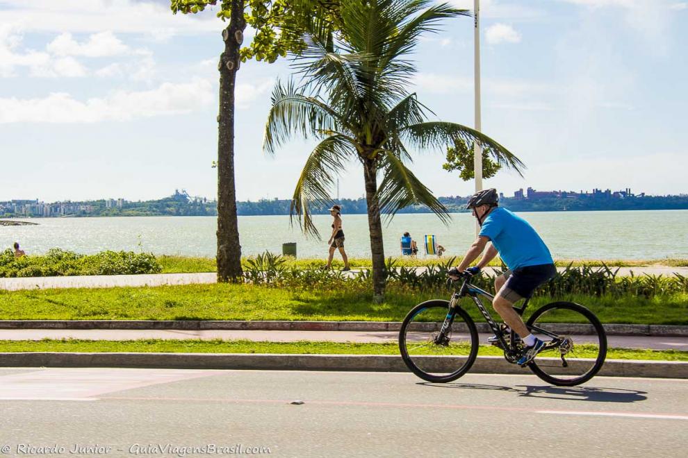 Imagem de um homem andando de bicicleta com capacete na avenida da praia.